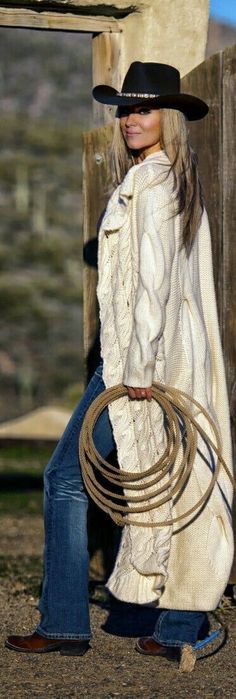 Woman in a cowboy hat, cable knit sweater, and jeans holding a rope outdoors