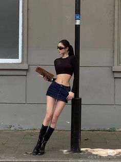 Woman in a black crop top and denim mini skirt leaning against a lamppost