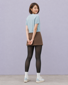Woman with short brown hair in a cropped top and mini skirt with black tights