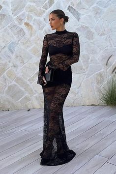 Woman in a black lace dress and gold earrings holding a clutch bag