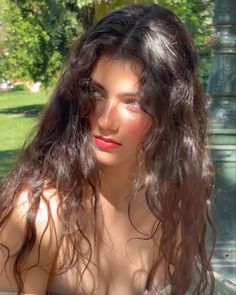 Woman with long wavy hair and red lipstick in sunlight outdoors