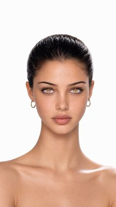 Woman with dark hair pulled back and gold hoop earrings on a white background