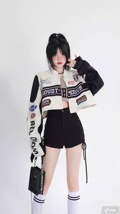 Woman in a racing jacket, crop top, and black shorts posing against a white background