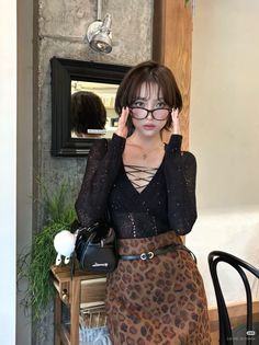 Woman with short hair and glasses wearing a lace-up top and leopard print skirt