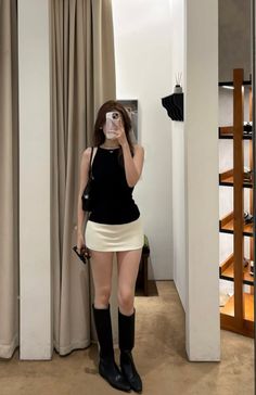 Woman in a black top and white mini skirt taking a mirror selfie