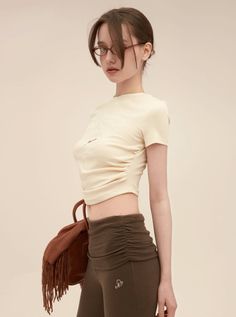 Woman in a cream crop top and brown ruched pants with glasses