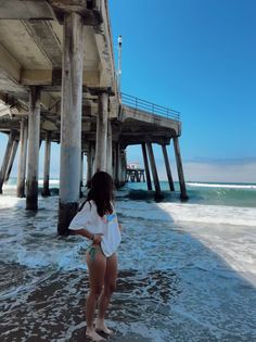 Woman in a bikini and t-shirt standing in the ocean under a pier