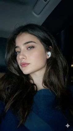 Woman with long dark hair and green eyes wearing wireless earbuds and a blue sweater