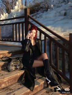 Woman with red hair in a leather coat and boots sitting on wooden steps in winter