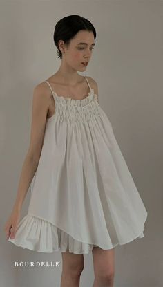 Woman with short hair wearing a white smocked dress with ruffle trim