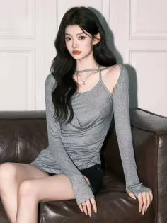 Woman with long dark hair wearing a gray top and black shorts, sitting on a couch