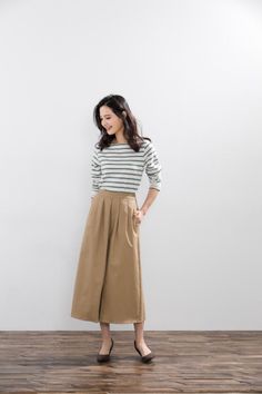 Woman in a striped shirt and wide leg pants standing against a white wall