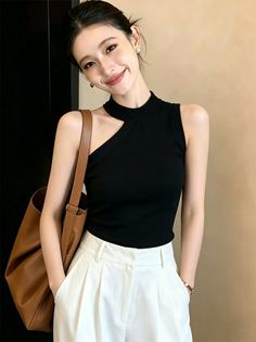 Woman in a black top and white pants with a brown bag, smiling at the camera