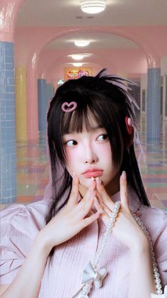 Woman with long black hair and pink blush holding a pearl necklace indoors