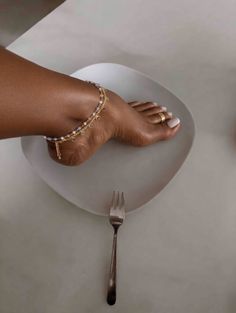 Foot with an anklet and toe ring on a white plate with a fork