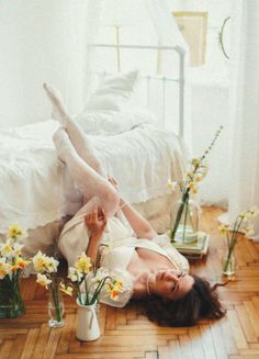 Woman in a white dress and stockings lying on a wooden floor surrounded by daffodils