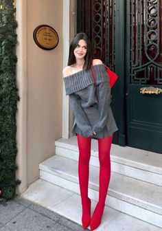 Woman in an off-shoulder sweater, mini skirt, and red tights standing outdoors