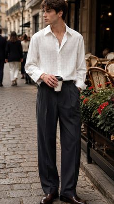 Man in a white shirt and black pants holding a coffee cup on a cobblestone street