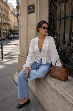 Woman in a white blouse and blue jeans sitting on a ledge on a city street