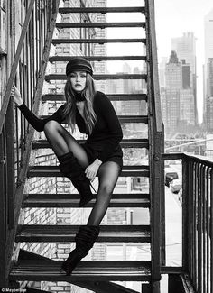 Woman in a black dress and boots posing on a fire escape in a city