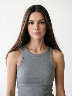 Woman with long brown hair wearing a gray tank top against a white background
