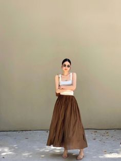 Woman in a white tank top and long brown skirt posing outdoors