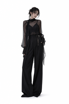 Woman in a black sheer top and wide-leg pants with a cross necklace