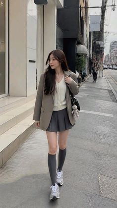 Woman in a blazer and pleated skirt walking on a city street