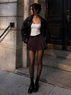 Woman in a black leather jacket and pleated skirt standing on a street