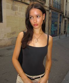 Woman with long dark hair wearing a black tank top and gold jewelry on a street
