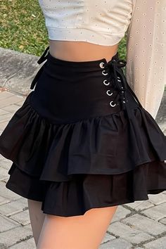 Person wearing a black ruffle skirt with lace-up detail and a white crop top