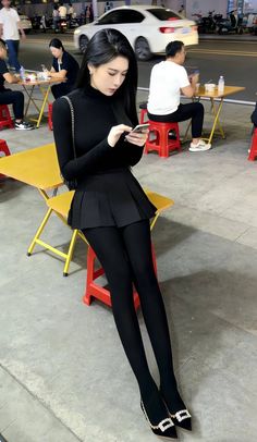 Woman in a black turtleneck and pleated skirt sitting outdoors at night