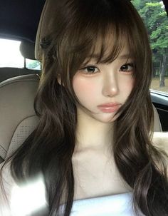 Woman with long wavy hair and bangs in a car, wearing a white tube top