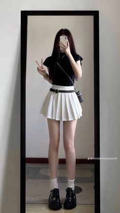 Person in a black top and white pleated skirt taking a mirror selfie