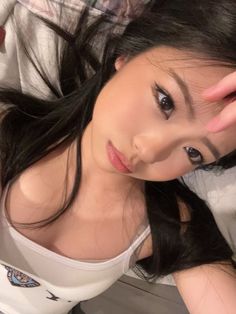Woman with long black hair wearing a white tank top, looking up at the camera
