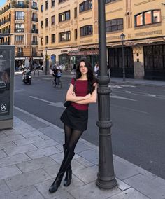 Woman in a red top and black skirt leaning against a lamppost on a city street