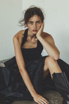 Woman with messy bun and freckles wearing a black dress, sitting indoors