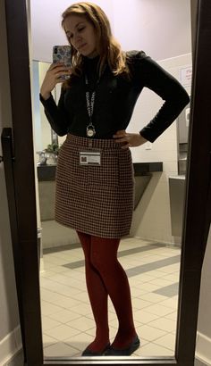 Woman in a black turtleneck, houndstooth skirt, and red tights taking a mirror selfie