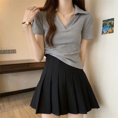 Person in a grey ribbed shirt and black pleated mini skirt indoors