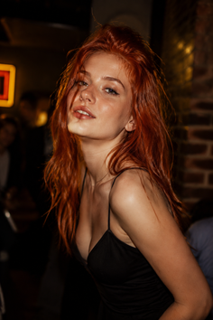 Woman with long red hair in a black dress in a dark indoor setting