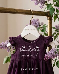 Purple baby dress with ruffle sleeves on a hanger surrounded by lilac flowers