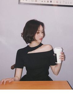 Woman with short hair in a black cut-out top holding a cup indoors
