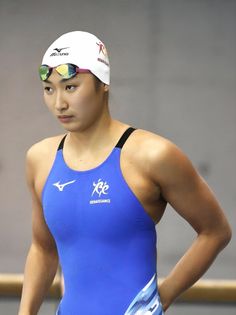 Female swimmer in a blue swimsuit, white cap, and goggles looking to the side