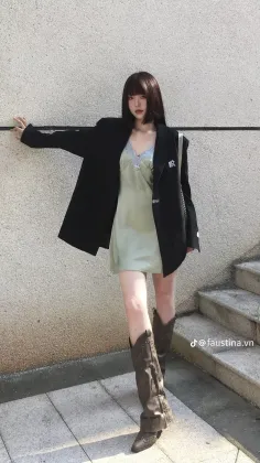 Woman in a black blazer and slip dress with cowboy boots leaning against a wall