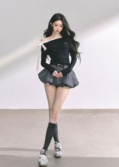 Woman with long black hair wearing an off-shoulder top and mini skirt indoors