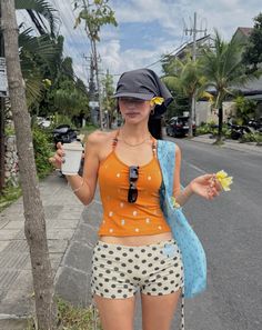 Woman in polka dot shorts and an orange top walking on a street