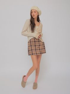 Woman in a beret, cardigan, and plaid skirt posing in a studio