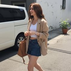 Woman with long hair wearing denim shorts and a blazer walking on a street