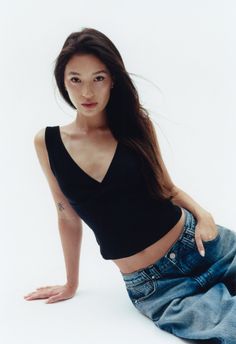 Woman with long dark hair wearing a black top and loose jeans in a studio