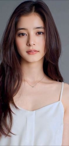 Woman with long brown hair wearing a white top and a delicate necklace